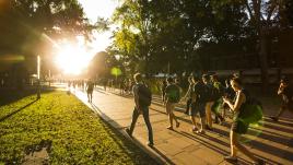 Students walking down the main walkway at UNSW, with the sun setting ahead of them